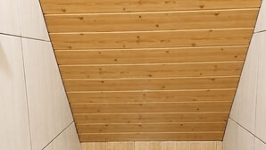 Een kleine, afgesloten badkamer met een houten plafond, een wit toilet en een betegelde vloer.
