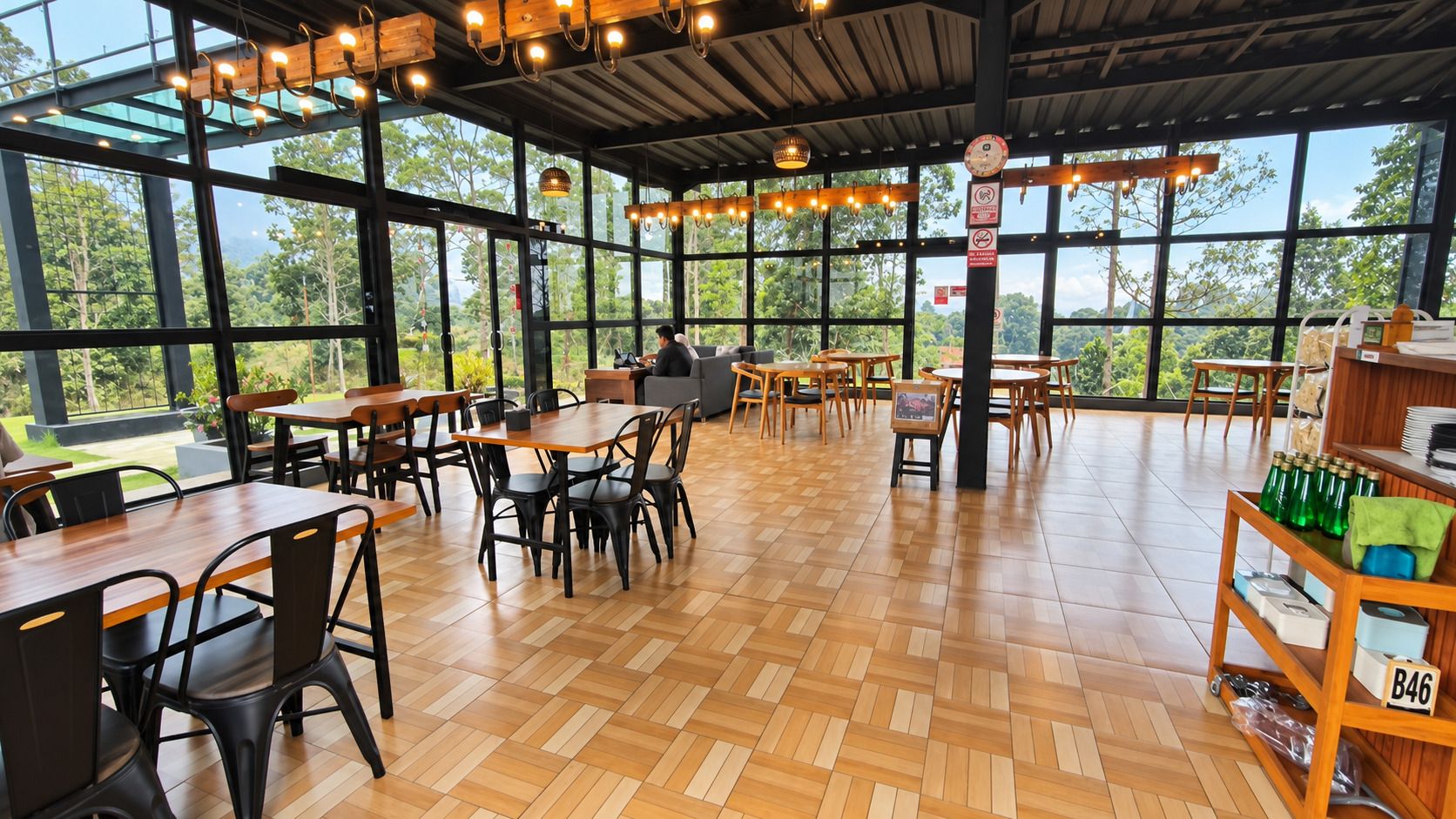 An indoor dining area with wooden tables and chairs, large windows, and a view of greenery outside.