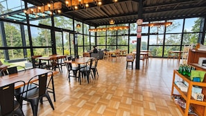 An indoor dining area with wooden tables and chairs, large windows, and a view of greenery outside. - Sakura Hills (Tawangmangu)