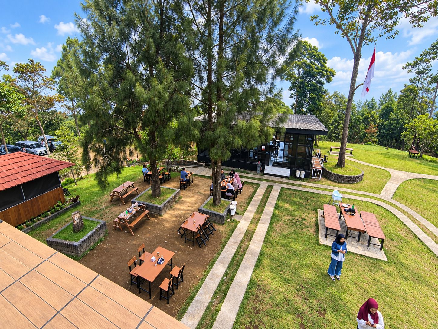 An outdoor dining area with multiple tables and chairs, surrounded by trees and a small building.