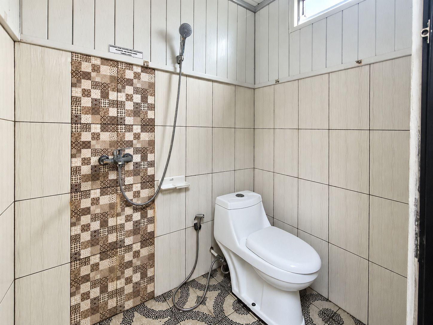 Un baño con pared de ducha con diseño, un inodoro y un cabezal de ducha.