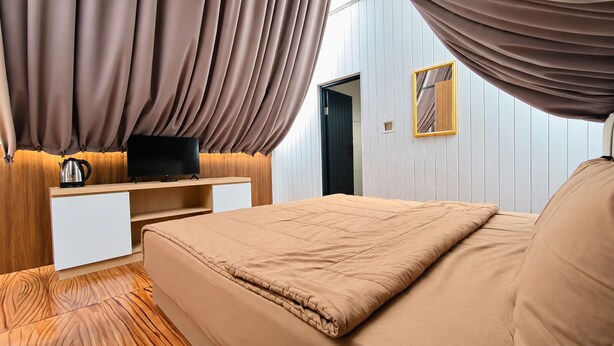 Een slaapkamer met een bed, een televisie op een houten dressoir en een raam met gordijnen.