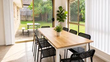 A dining area with a wooden table and black chairs, a potted plant, and a view of a backyard through a screened door.
