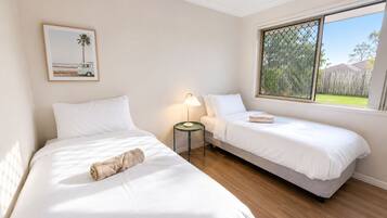 A bedroom with two single beds, a nightstand with a lamp, a framed picture on the wall, and a window with a view of the outdoors.