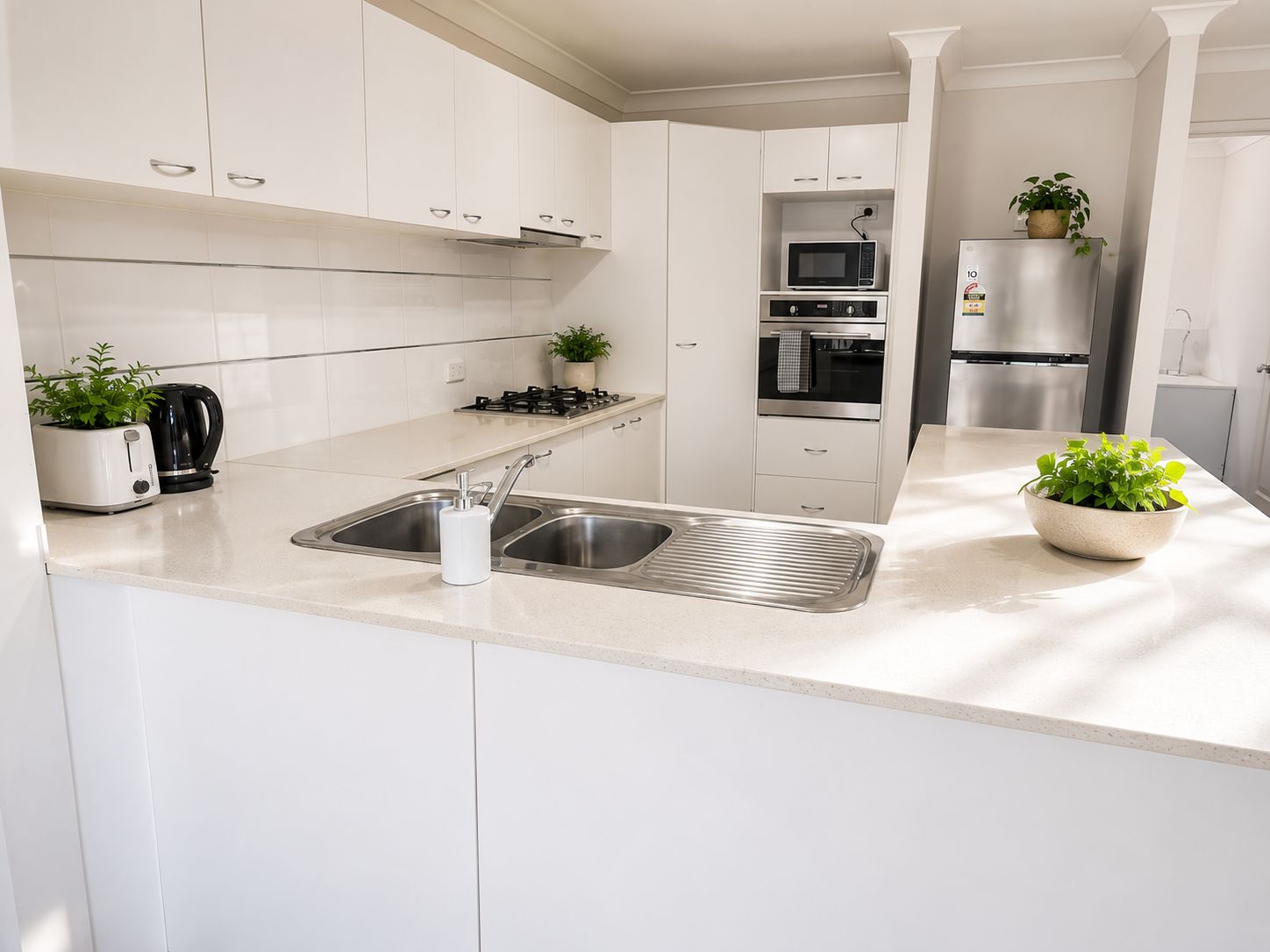 A modern kitchen with white cabinetry, a stainless steel sink, a microwave, an oven, and a refrigerator.
