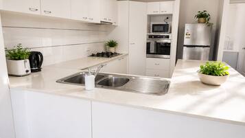 A modern kitchen with white cabinetry, a stainless steel sink, a microwave, an oven, and a refrigerator.
