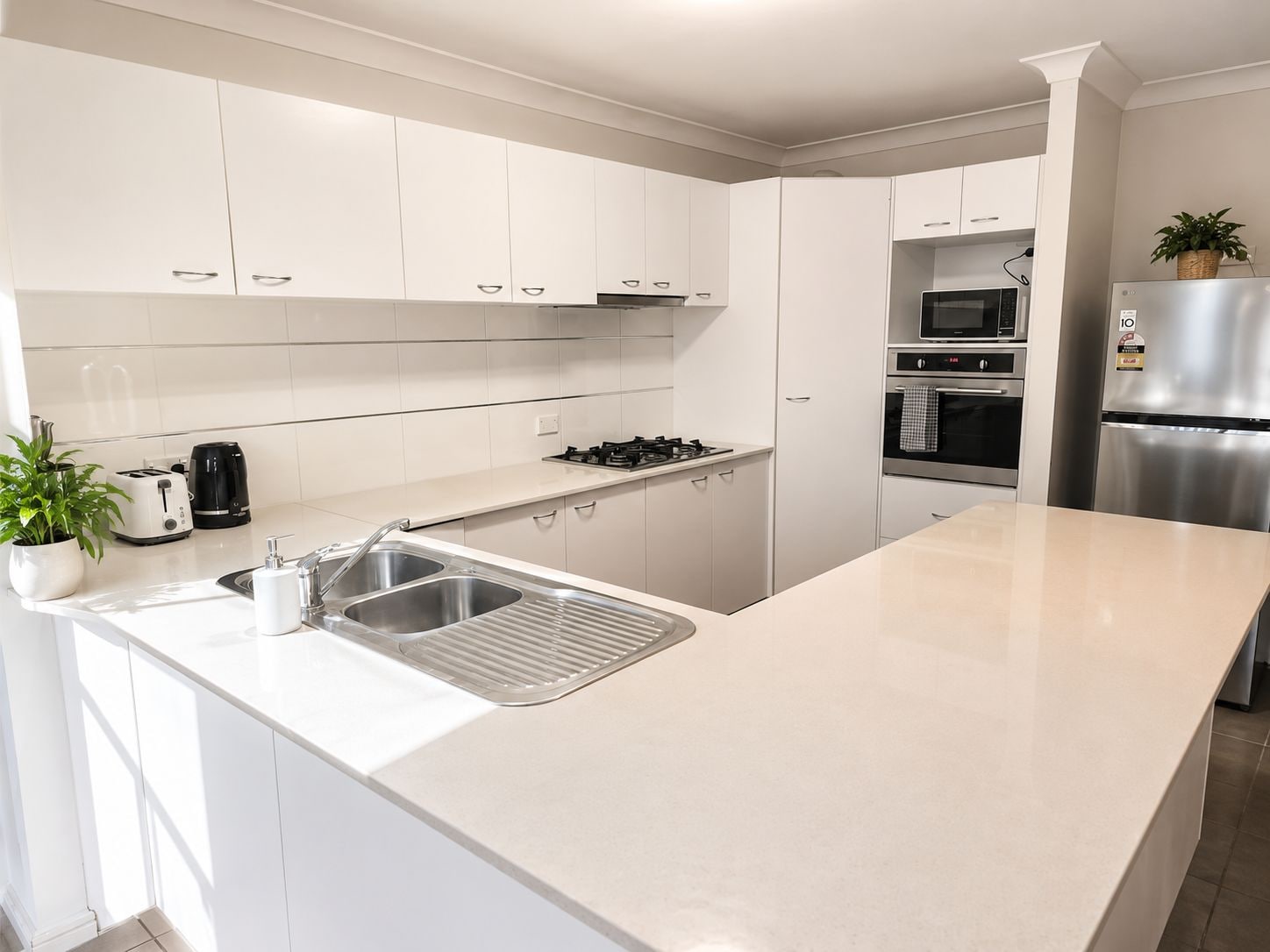 A modern kitchen with white cabinetry, a stainless steel sink, a gas stove, a microwave, and a refrigerator.