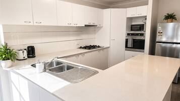A modern kitchen with white cabinetry, a stainless steel sink, a gas stove, a microwave, and a refrigerator.