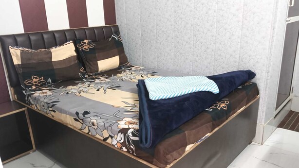 A bed with a floral bedspread, a headboard with a patterned design, and a blue blanket. - Indian Hotel and Restaurant (Bareilly)