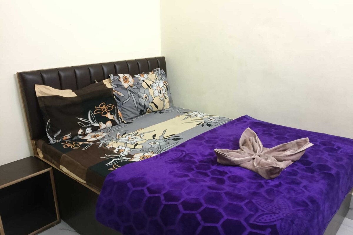 A bed with a floral bedspread, a purple blanket with a honeycomb pattern, and a folded towel on the bed.
