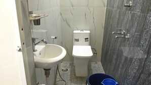 A compact bathroom with a white sink, toilet, and shower area. - Indian Hotel and Restaurant (Bareilly)