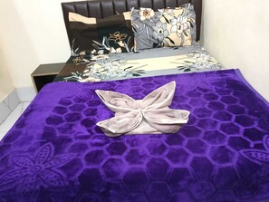A bed with a purple blanket and a decorative pillow. - Indian Hotel and Restaurant (Bareilly)