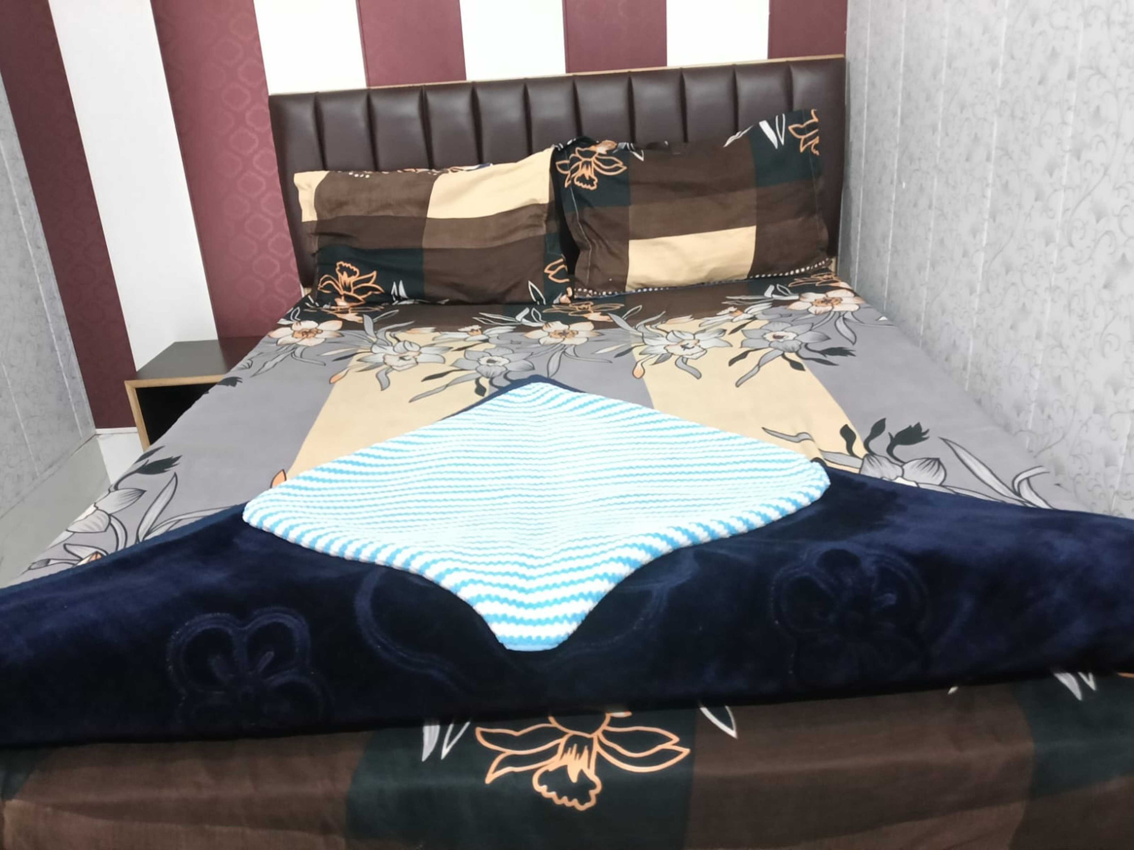 Una cama con cabecera, una colcha estampada con motivos florales y un cojín azul oscuro.