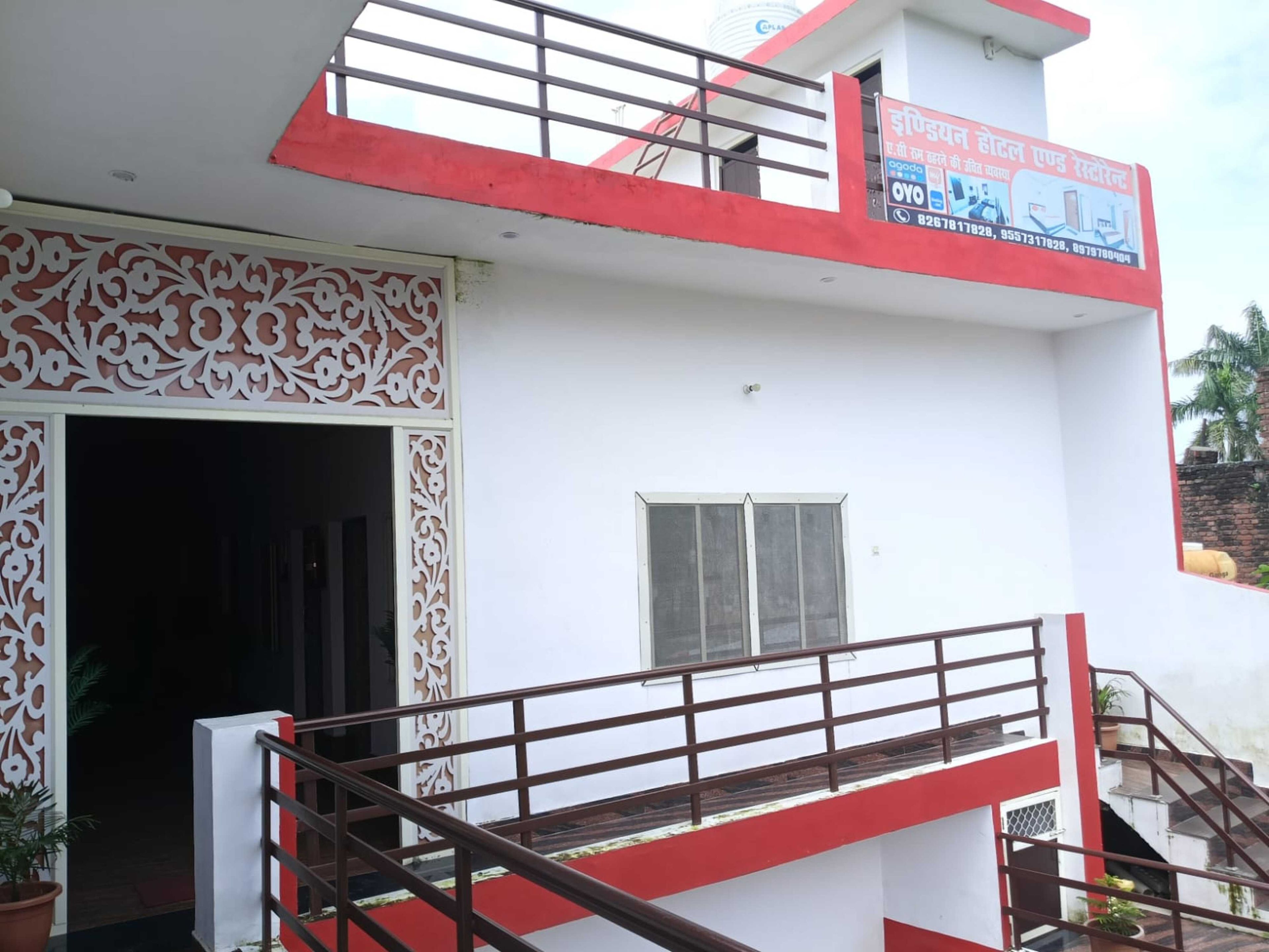 L’entrée d’un hôtel, agrémentée d’un portail décoratif, d’un escalier avec une rampe rouge et d’un panneau indiquant les coordonnées.