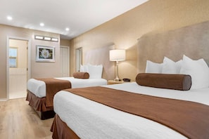 Habitación de hotel con dos camas, una mesita de noche con lámpara, un espejo y un cuadro en la pared.