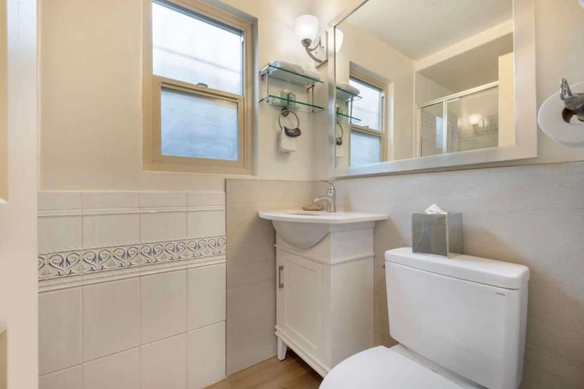 A bathroom with a toilet, sink, and mirror. There are windows and a towel rack.