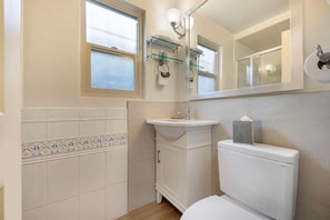 A bathroom with a toilet, sink, and mirror. There are windows and a towel rack. - Best Room At the Western (San Diego)