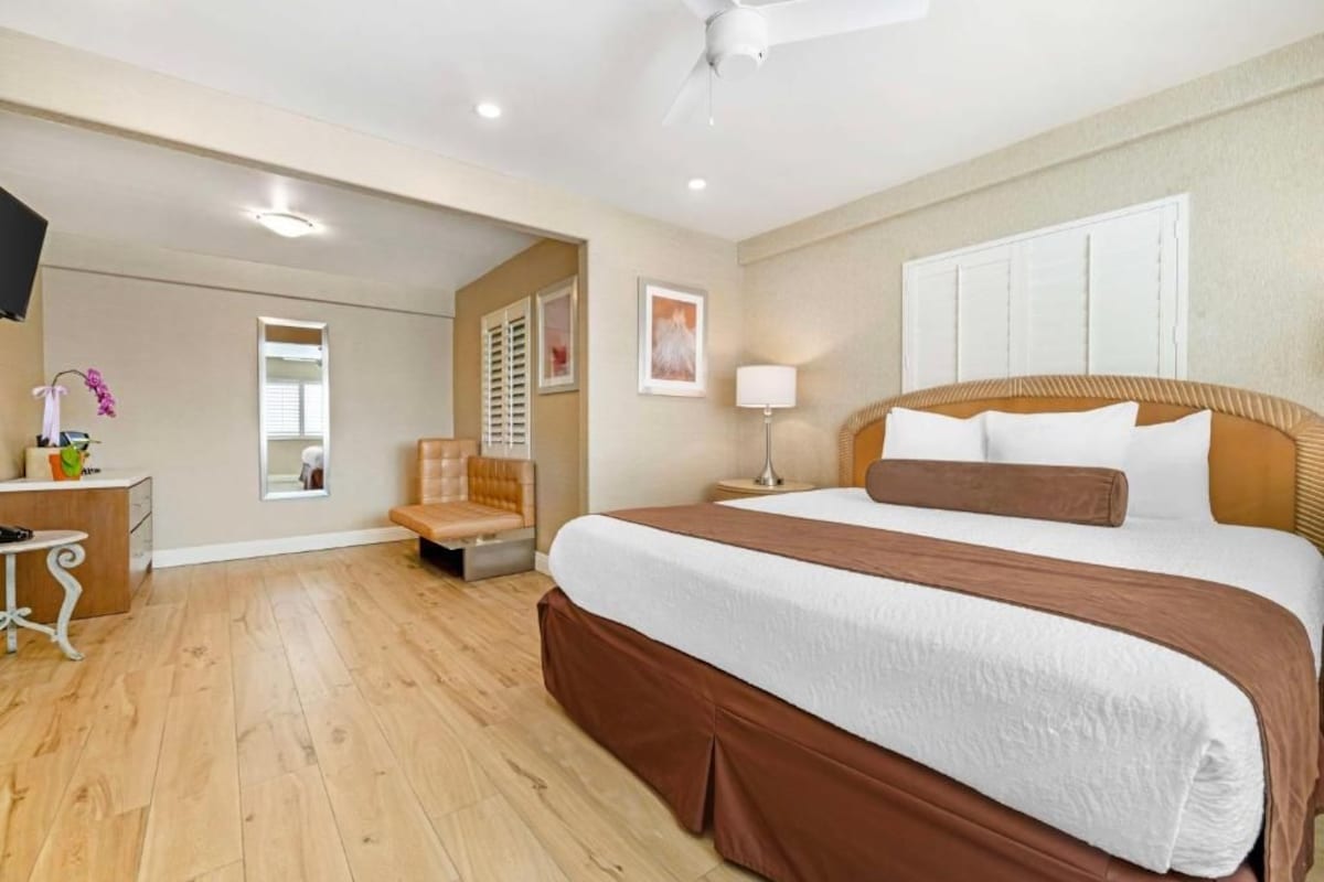 Habitación de hotel con una cama grande, una mesita de noche, una silla, un escritorio y un ventilador de techo.