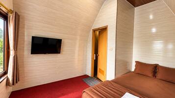 Ein Zimmer mit einem an der Wand montierten Flachbildfernseher, einer Holztür, einem roten Teppich und einem Bett mit braunen Bettwaren.