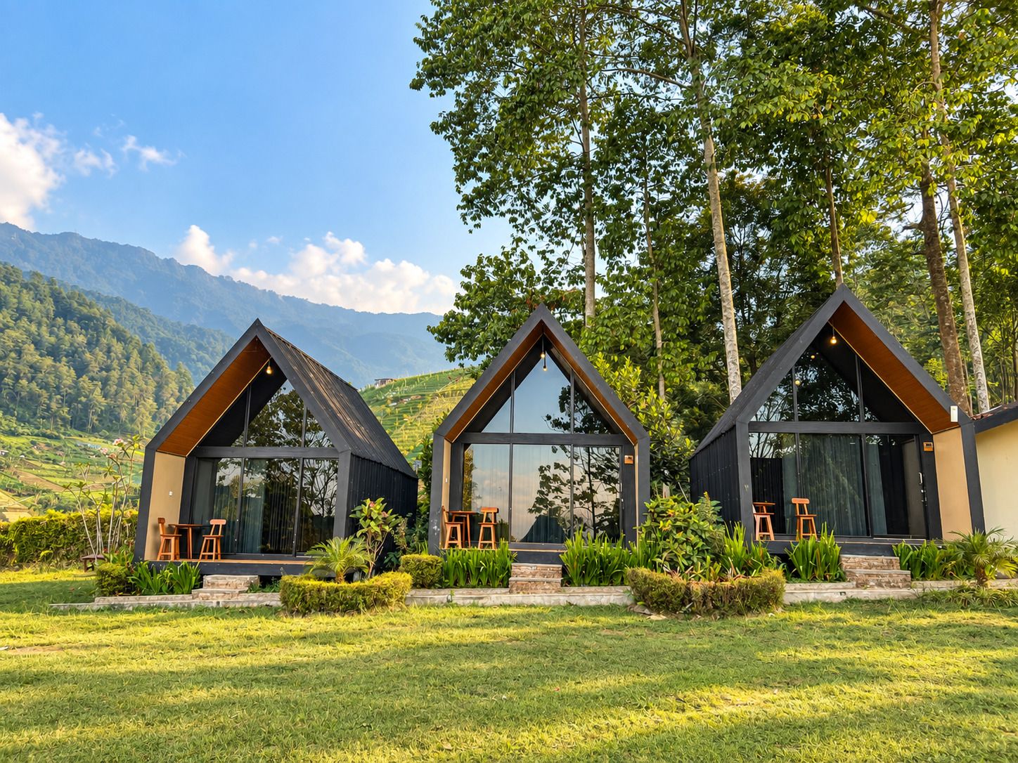 Three modern cabins with large windows, set in a lush green landscape with mountains in the background.