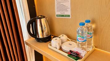Un plateau contenant une bouilloire en acier inoxydable, des bouteilles d’eau et des sachets de Nescafe, posé sur une surface en bois.