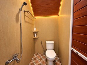 A small bathroom with a shower, toilet, and shelves with toiletries. - Tawangmangu Wonderpark (Tawangmangu)