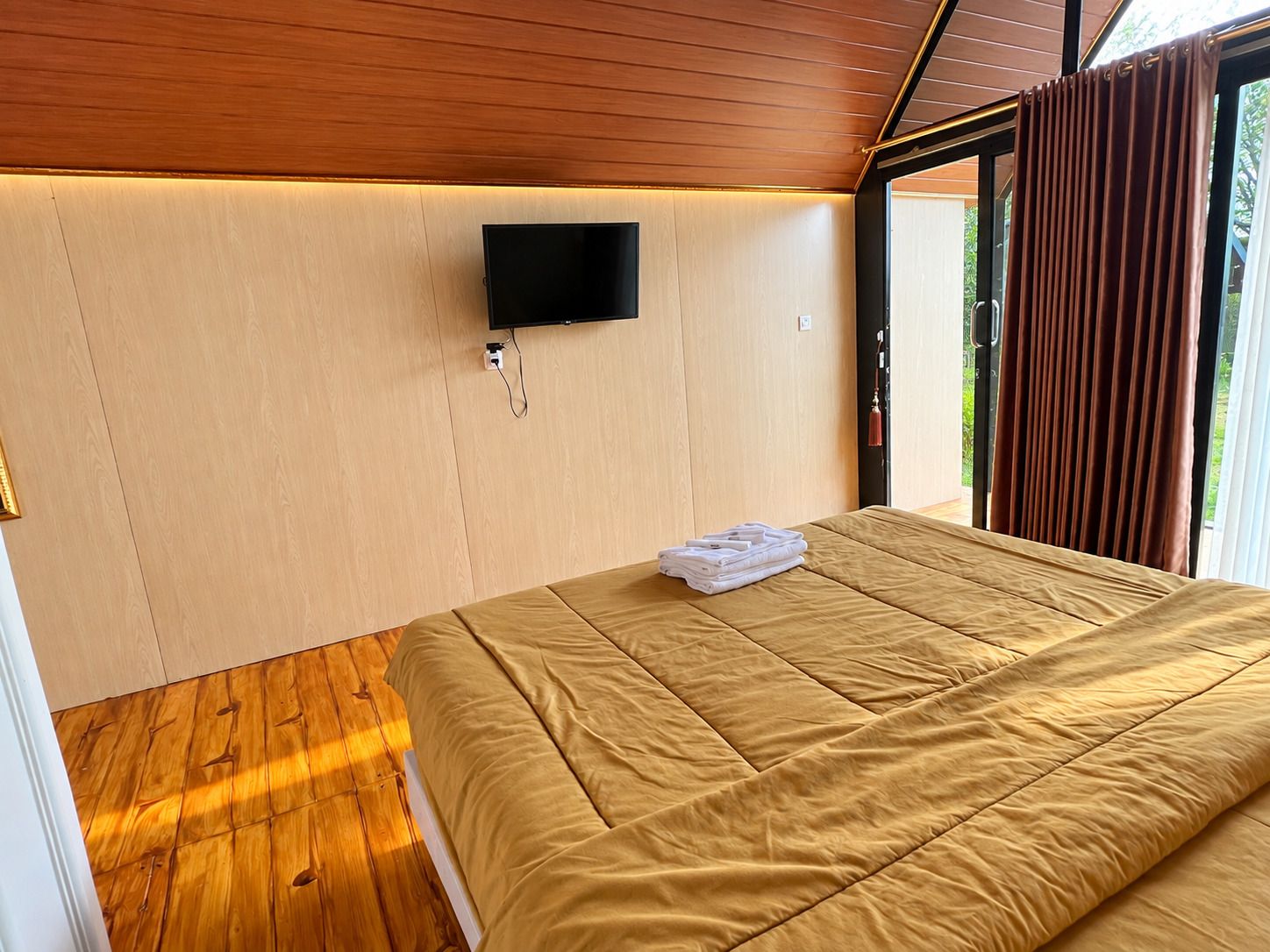 A bedroom with a bed, a television mounted on the wall, and a window with curtains.