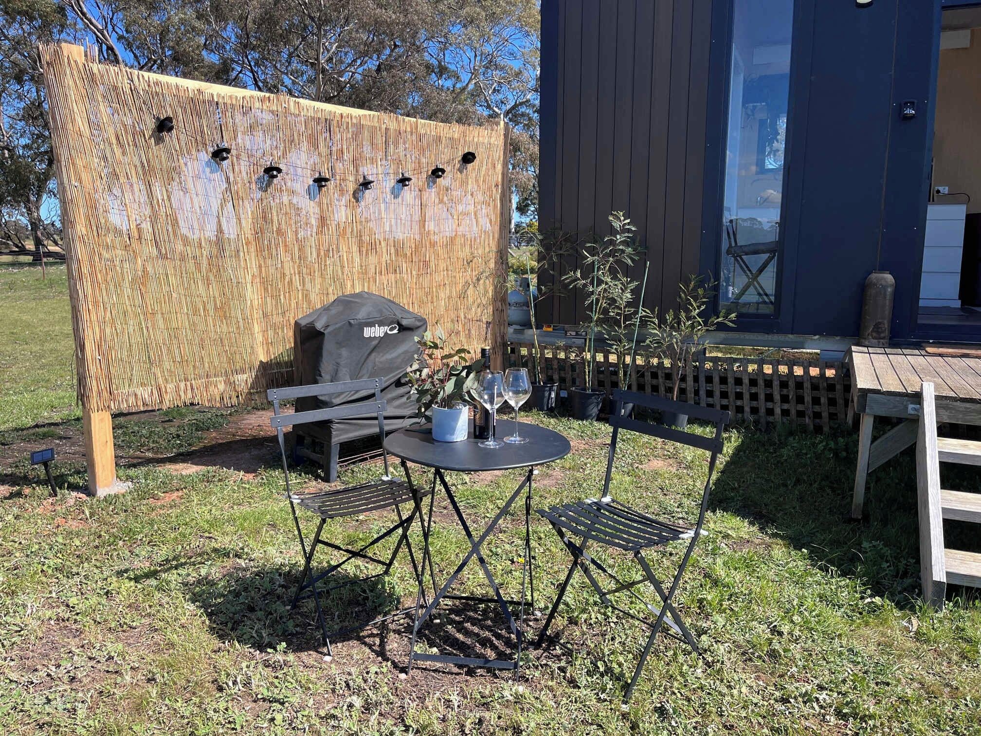 An outdoor seating area with a table and chairs, a grill, and a bamboo screen.