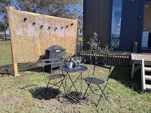 An outdoor seating area with a table and chairs, a grill, and a bamboo screen. - Stringybark by Tiny Away (Rhymney)