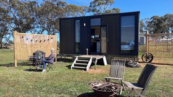 A modern, compact cabin with a large window, a small deck, and a fire pit in the yard.