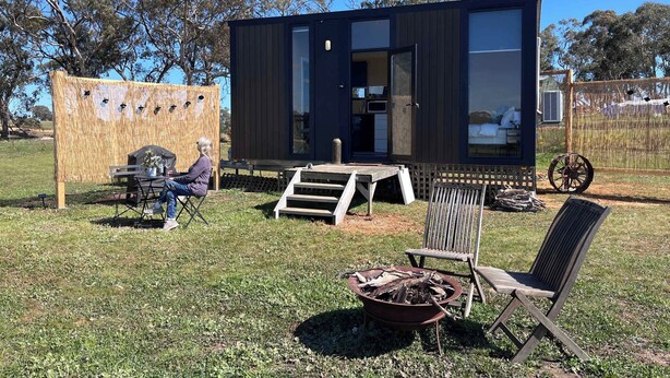 A modern, compact cabin with a large window, a small deck, and a fire pit in the yard. - Stringybark by Tiny Away (Rhymney)