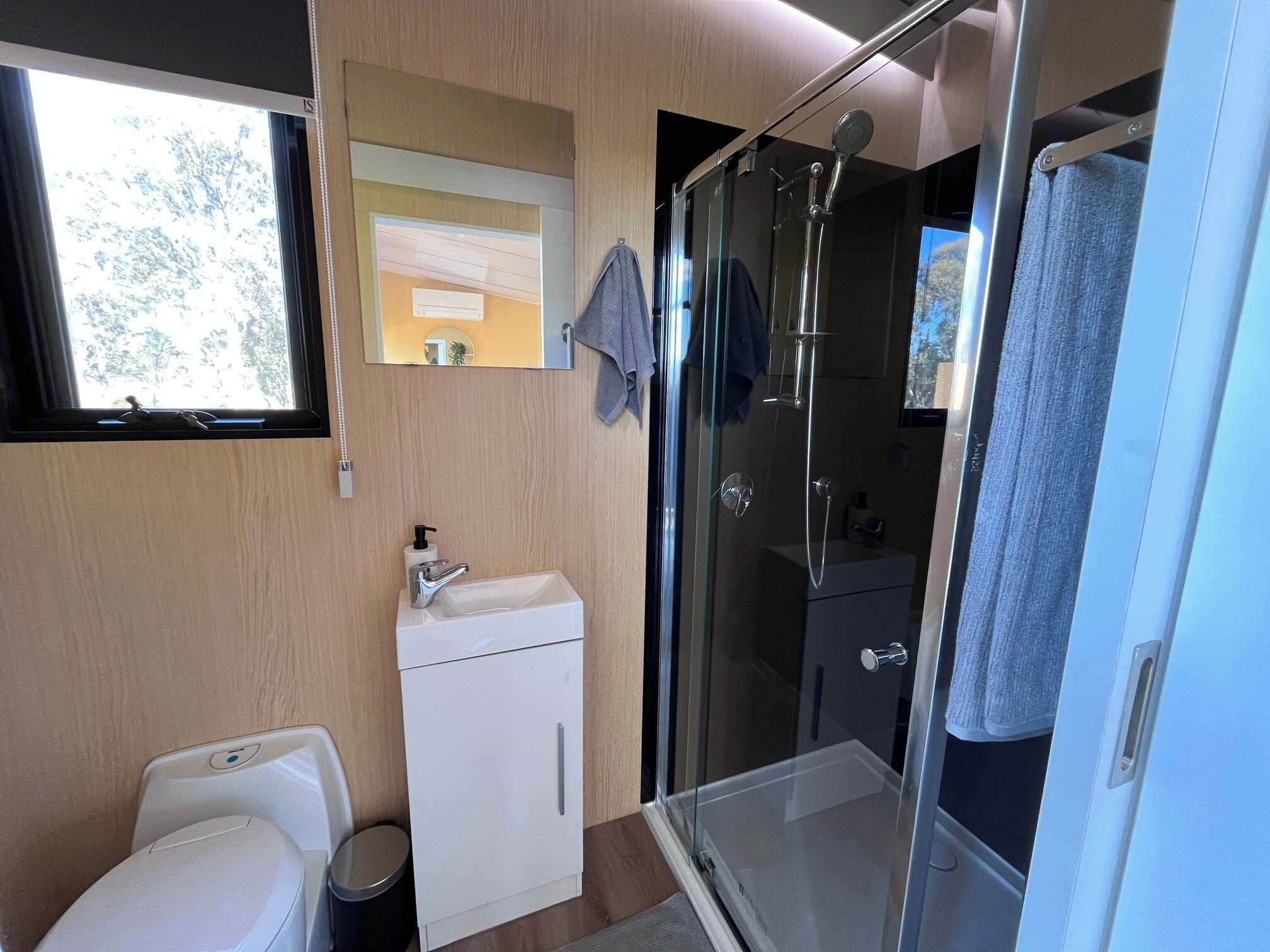 A modern bathroom with a glass shower enclosure, a sink with a soap dispenser, and a mirror above the sink.