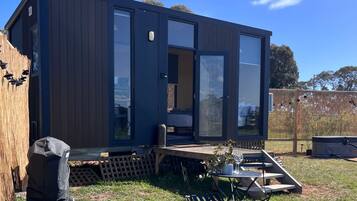 Une maison mobile moderne, de couleur sombre, dotée de grandes portes vitrées, d’une petite terrasse et d’un espace patio avec une table et des chaises.