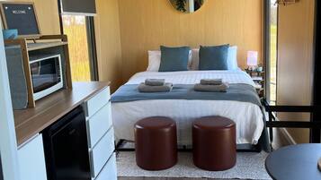 Een moderne slaapkamer met een bed, nachtkastjes, een magnetron, een spiegel en uitzicht op het groen.