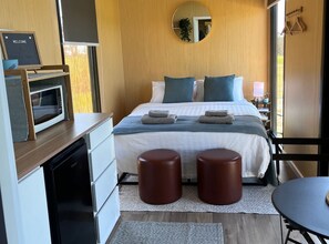 Une chambre moderne équipée d’un lit, de tables de chevet, d’un four à micro-ondes, d’un miroir et offrant une vue sur l’extérieur.