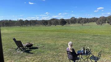 An outdoor seating area with a table and chairs, a grill, and a view of a grassy field with trees.