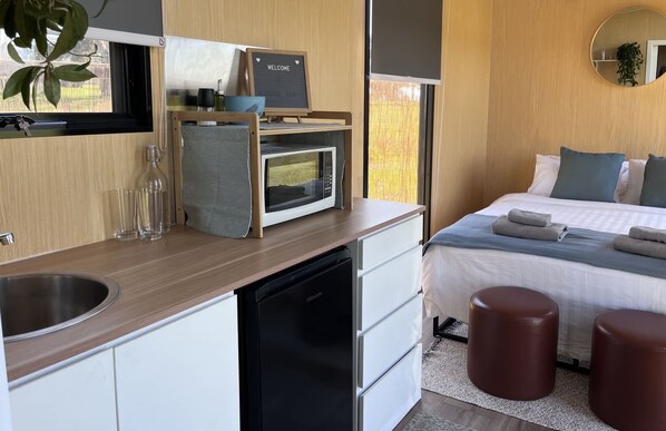 A modern bedroom with a bed, bedside tables, a small desk, and a microwave.