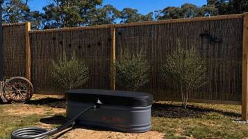 Un réservoir d’eau noir avec un tuyau, une clôture en bois et deux petits arbres dans un jardin.