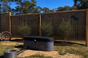A black water tank with a hose, a wooden fence, and two small trees in a backyard.