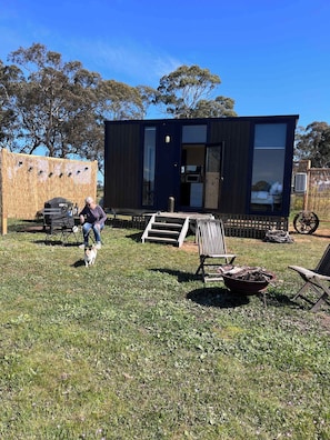 A modern, dark-colored cabin with a large window, a wooden deck, and a grill set up outside. - Stringybark by Tiny Away (Rhymney)