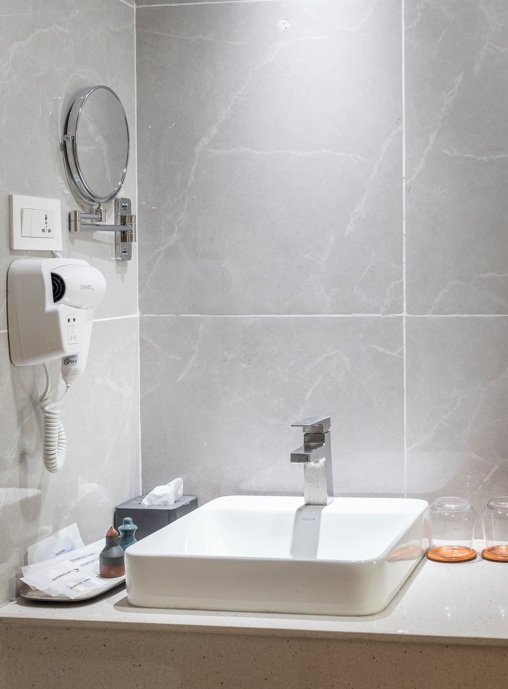 Un baño con lavamanos blanco, espejo, secador de pelo y toallero.