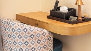 Habitación de hotel con un escritorio de madera, una silla estampada, un control remoto, una caja de pañuelos, una lámpara y un cartel de 'No Fumar'.