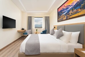 A hotel room with a bed, a desk, a chair, a TV, a window with curtains, and a painting on the wall. - HOTEL DAAAS KATHMANDU (Kathmandu)