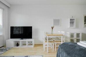 A room with a television on a white cabinet, a dining table with chairs, and a cabinet with glass doors. - City Station Flat By Lapland Host (Rovaniemi)