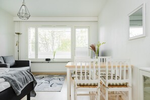 Een slaapkamer met een bed, een bureau en een ledikant. Er zijn ramen met jaloezieën, een radiator en een hanglamp.