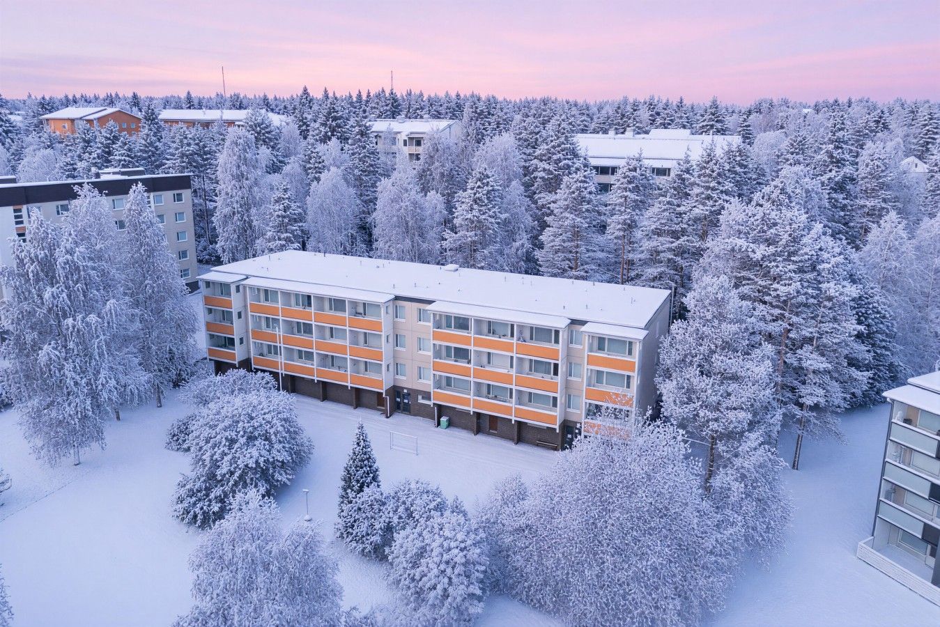 A multi-story building with a modern design, surrounded by snow-covered trees and a clear sky.