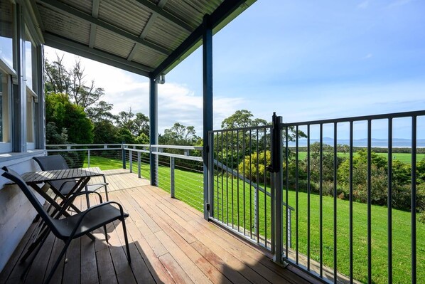 Un espace extérieur abrité doté d’une terrasse en bois, d’une rambarde en métal et offrant une vue sur un paysage verdoyant.