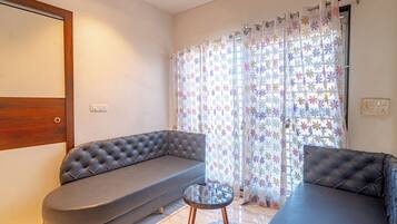 Ein Wohnzimmer mit grauem Sofa, einem runden Couchtisch und einem Fenster mit blumigen Vorhängen.