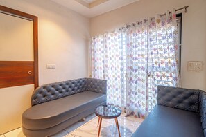 Una sala de estar con un sofá gris, una mesa de centro redonda y una ventana con cortinas florales.