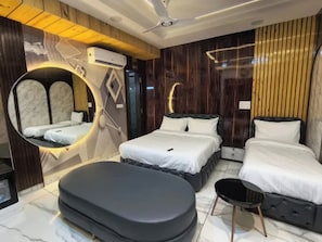 A modern hotel room with a large bed, a smaller bed, a seating area, and a unique circular mirror. - LAKSHYA HOTEL AND RESTAURANT (Ujjain)